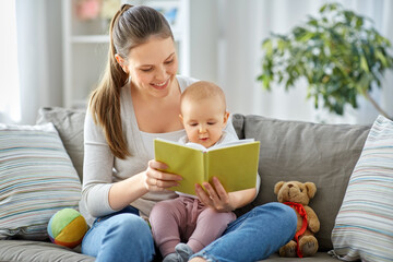 family, motherhood and people concept - happy smiling mother reading book to little baby daughter at home