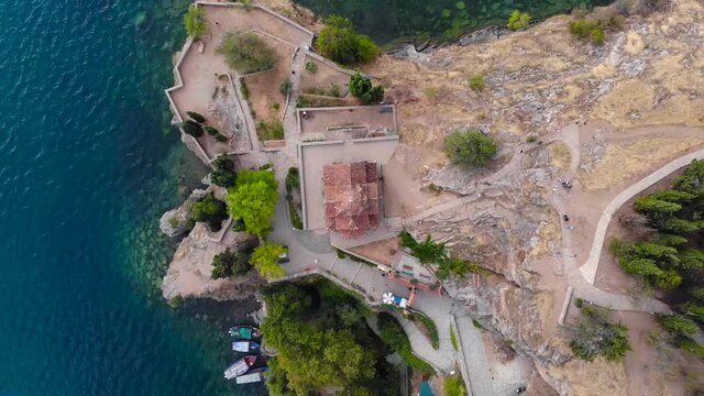 An gothic old orthodox church at coast of lake Ohrid. Beautiful medieval architecture, forest and emerald colored water. Vertical shot of aerial drone took with 4K 30fps.