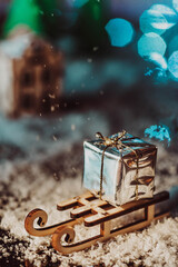 sledges in the snow are carrying a shiny box with a gift. wooden sledges on white fluffy snow against a background of bright lights and houses