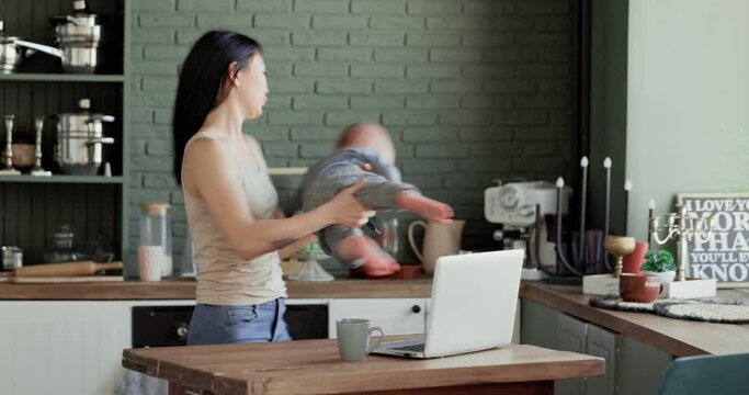 Freelance woman with a small child tries to work on a laptop in the kitchen. Home business concept.