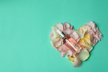 Essential rose oil and rose petals on mint background