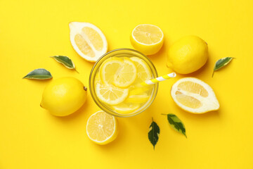 Glass of lemonade and lemons on yellow background