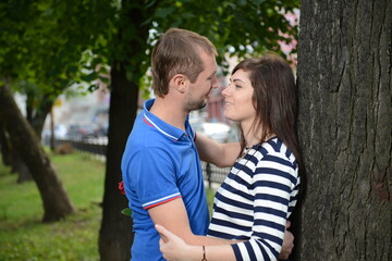 The guy and the girl look at each other hugging a tree. - 435790646