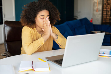 Overworked African-American freelancer woman feels eyes strain due to long-term work with a laptop,...