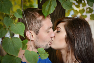 Kissing young people framed by green leaves. - 435792203