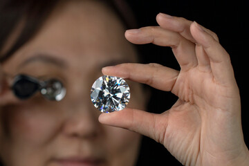 Close up of round cut diamond in hand of asian woman evaluating the quality of diamond through...