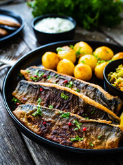 Fried herring fillets with potatoes and vegetable salad  on wooden table
