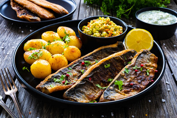 Fried herring fillets with potatoes and vegetable salad  on wooden table
