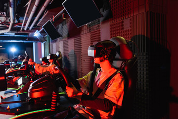 Fototapeta na wymiar teenage gamers in vr headsets racing on car simulators in play zone
