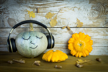 Pumpkin music lover with a funny face in headphones on a wooden background with autumn leaves. The...