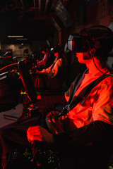 teenager in vr headset racing on car simulator near blurred friends