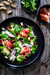 Tasty salad - ham, parmesan and fresh vegetables on wooden background
