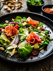 Tasty salad - ham, parmesan and fresh vegetables on wooden background
