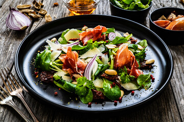 Tasty salad - ham, parmesan and fresh vegetables on wooden background
