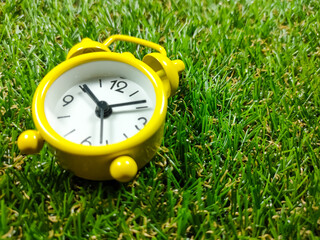 Alarm clock on grass background. Time concept. Yellow alarm clock with fresh green grass with copy...