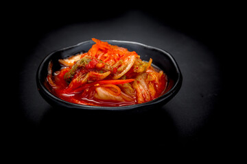 Kimchi on black dish on black background. Kimchi is the national dish of Koreans That is more popular, Kimchi making is a type of food preservation method. By using salt to ferment with white cabbage.