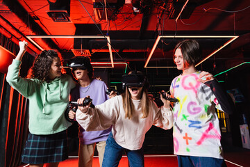 african american teenage girl showing triumph gesture near amazed friends in vr headsets