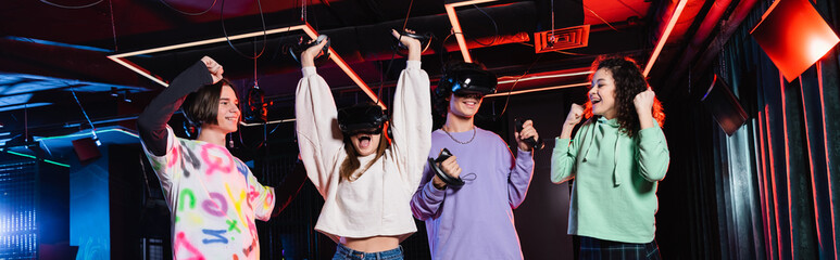 excited multiethnic teenagers showing win gesture in vr game zone, banner
