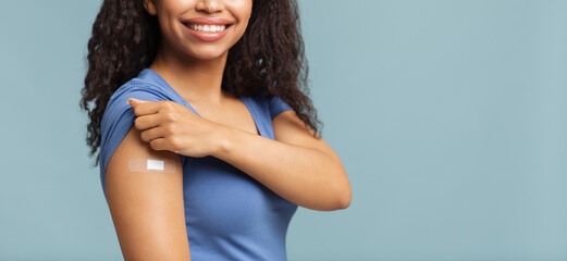 Successful covid-19 vaccination. Happy unrecognizable black woman showing arm with plaster, blue...