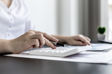 Close-up of woman holding a pen and pressing a white calculator, a corporate finance auditor examining the numbers on financial documents prepared by the finance department to bring to the meeting.