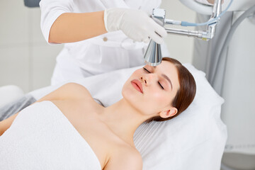 Obraz na płótnie Canvas Cosmetologist treating face of woman with laser machine