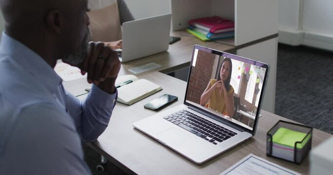 African american senior man having a video call with female colleague on laptop at office