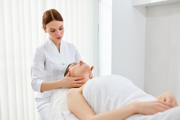 Obraz premium Therapist or cosmetologist doing myofascial or buccal massage on face, head and neck for female client lying at spa salon