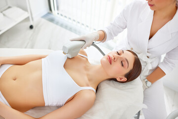 Cosmetologist treating neck, decollete area and chest of woman with laser machine