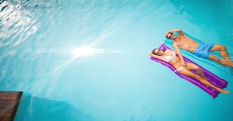Composition of couple lying on inflatables in swimming pool with glowing light and copy space