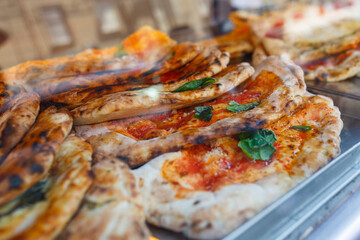 Ripieni cotti al forno con all'interno salame, ricotta e mozzarella e all'esterno sugosi pomodoro e basilico in esposizione in una vetrina di una pizzeria