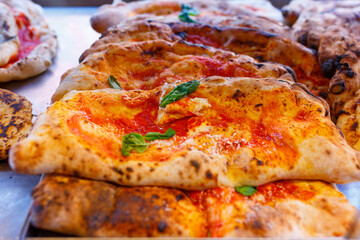 Ripieni cotti al forno con all'interno salame, ricotta e mozzarella e all'esterno sugosi pomodoro e basilico in esposizione in una vetrina di una pizzeria