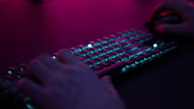 Gamer dude playing computer games on blue lit gaming keyboard.