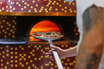 Pizza margherita napoletana con sugo di pomodoro, mozzarella di bufala e basilico mentre viene infornata in un tradizionale forno a legna