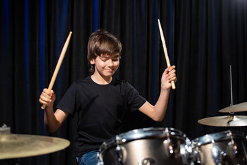 The boy learns to play the drums in the studio on a black background. Music school student