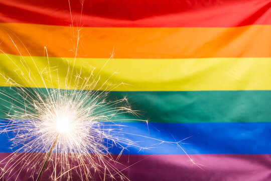 Glowing sparkler against waving LGBT flag with copy space