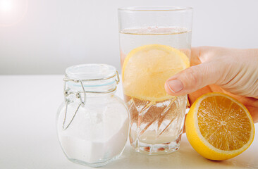 Hand holding drinking glass with baking soda, water and lemon juice infusion, health benefits for...