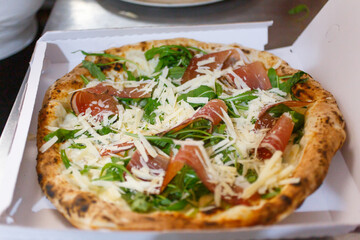 Pizza napoletana con mozzarella di bufala, speck, rucola e formaggio a scaglie in un cartone d'asporto per la pizza