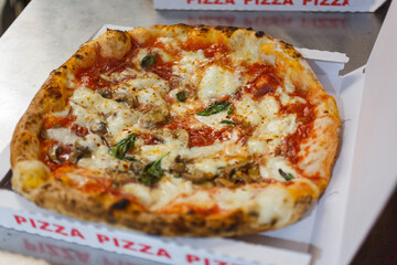 Pizza napoletana con sugo di pomodoro, mozzarella di bufala, funghi e basilico mentre viene chiusa in un cartone d'asporto per le pizze