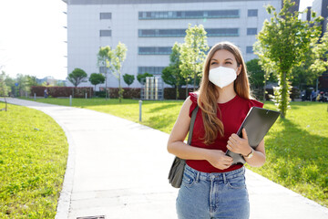 Business girl with protective mask walks holding folders in her hands with office buildings on the background