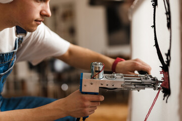 Young white man in headphones working on craft rug with sewing machine