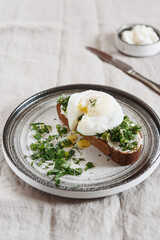 Healthy Breakfast with Poached Egg on toast with cream cheese and chopped mix of green onions, dill and parsley on greige linen tablecloth