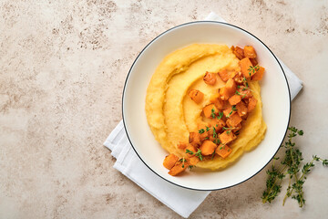 Polenta with butter, pumpkin, garlic, savory and parmesan cheese in white bowl on light concrete background. Traditional Basic Italian food, vegan food. Top view. Copy space.