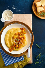 Polenta with butter, pumpkin, garlic, savory and parmesan cheese in white bowl on dark blue concrete background. Traditional Basic Italian food, vegan food. Top view. Copy space.