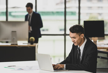 Asian man working on laptop in office with colleague