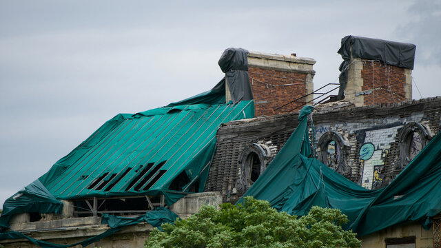 Side view of a dilapidated roof of an old building with two chimneys, graffiti on the walls and some tarp laid out as protection