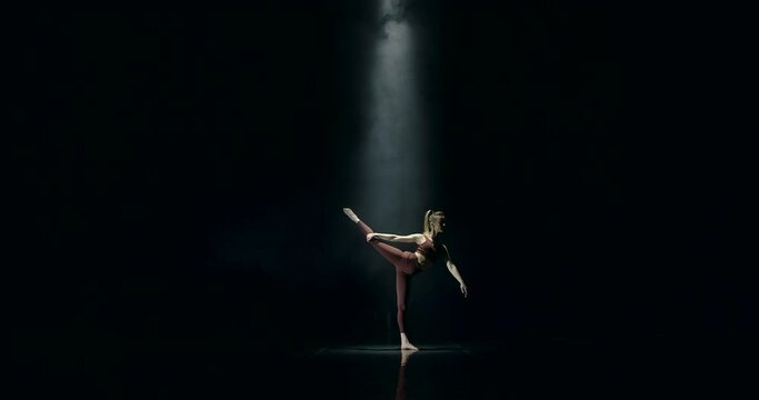 A young and feminine gymnast stretches in the light of a lonely lantern. She slowly makes the swallow element, after which she raises her leg into a split, she helps herself with her hand
