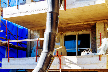 Suspended sections of black garbage chute on a facade of building under construction, Debris Chutes