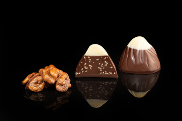 Chocolate candies on a dark background with reflection. Piece by piece and as a whole. Filling of nuts and fruits.