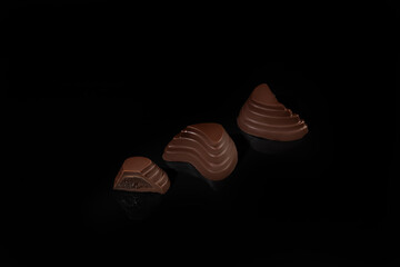 Chocolate candies on a dark background with reflection. Piece by piece and as a whole. Filling of nuts and fruits.