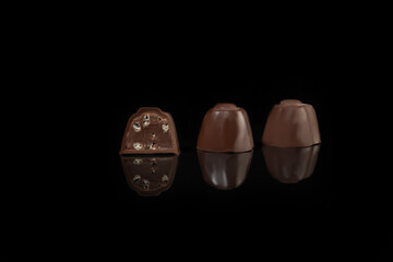 Chocolate candies on a dark background with reflection. Piece by piece and as a whole. Filling of nuts and fruits.